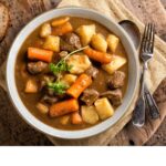 classic beef stew flat lay with rustic silverware and worn rustic wood table
