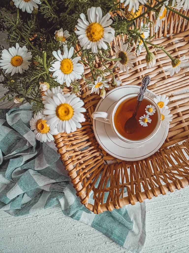 Enjoying simple ways to reconnect. A cozy flatlay featuring chamomile tea in a cup, surrounded by fresh chamomile flowers on a wicker basket.
